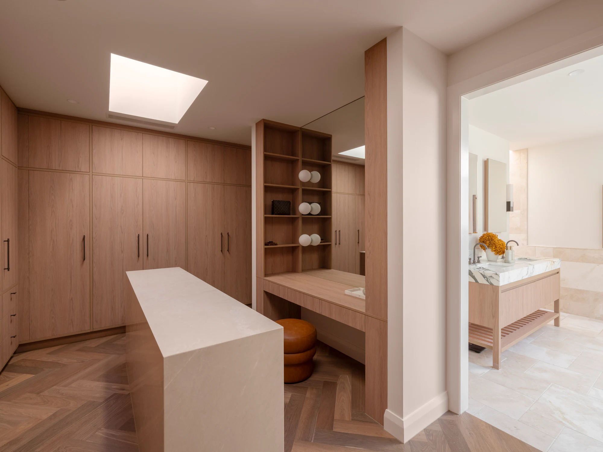 Timber wardrobes and a stone island beside the adjoining bathroom on the right, with a marble vanity, lighting and tiled floor.
